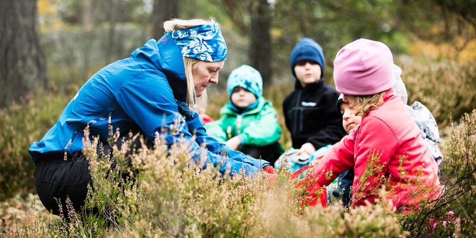 Pedagog sitter med förskolebarn i skogen